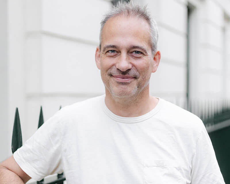 Smiling man wearing a white t-shirt stood in front of railings