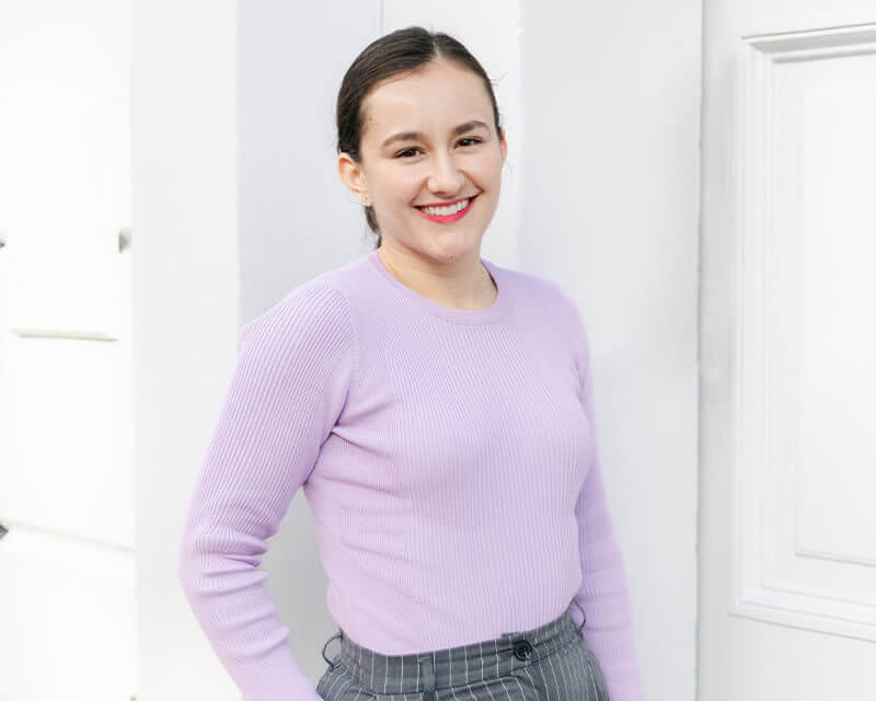Smiling woman wearing lilac top stood in a doorway