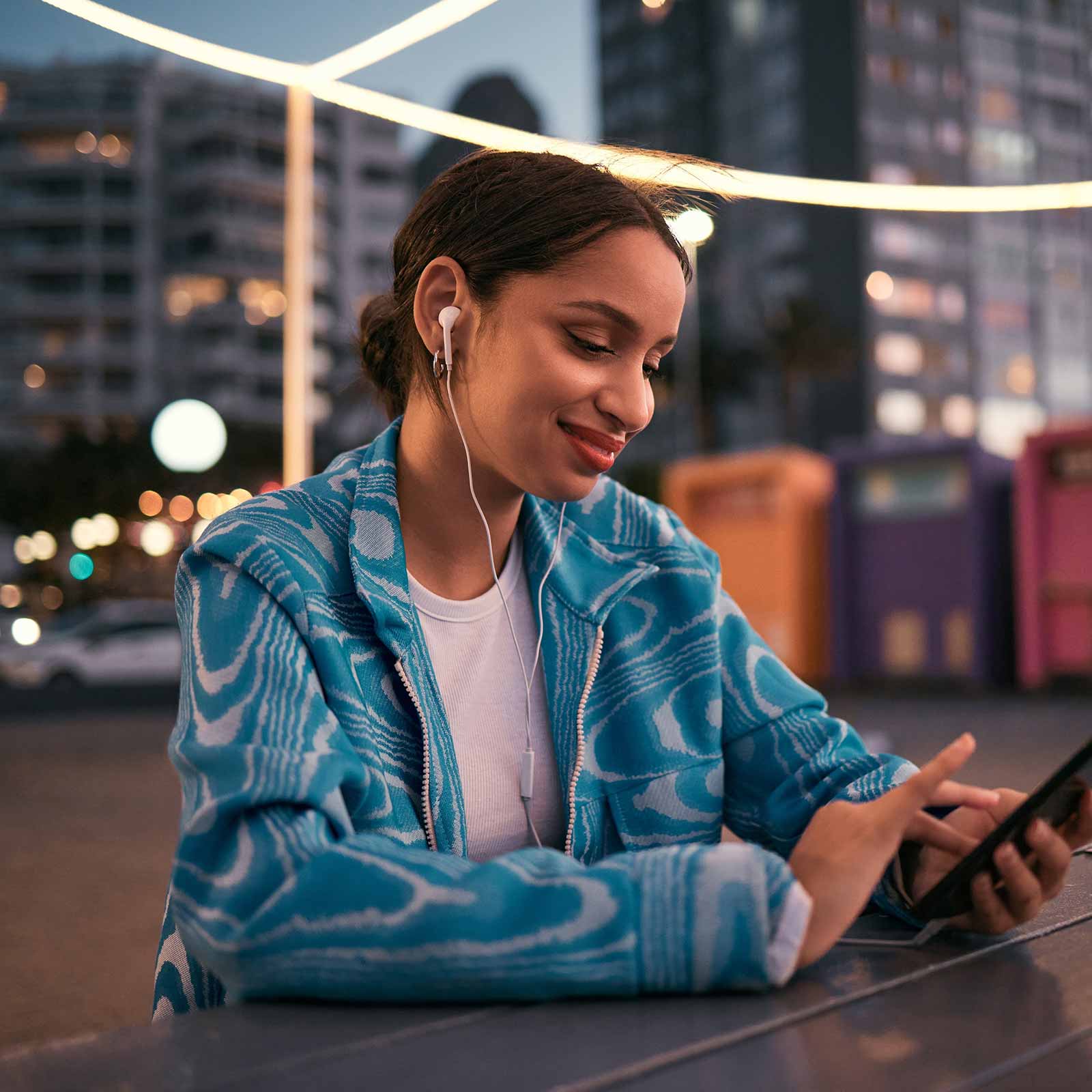 Woman looking wearing headphones using a phone sitting outside at night