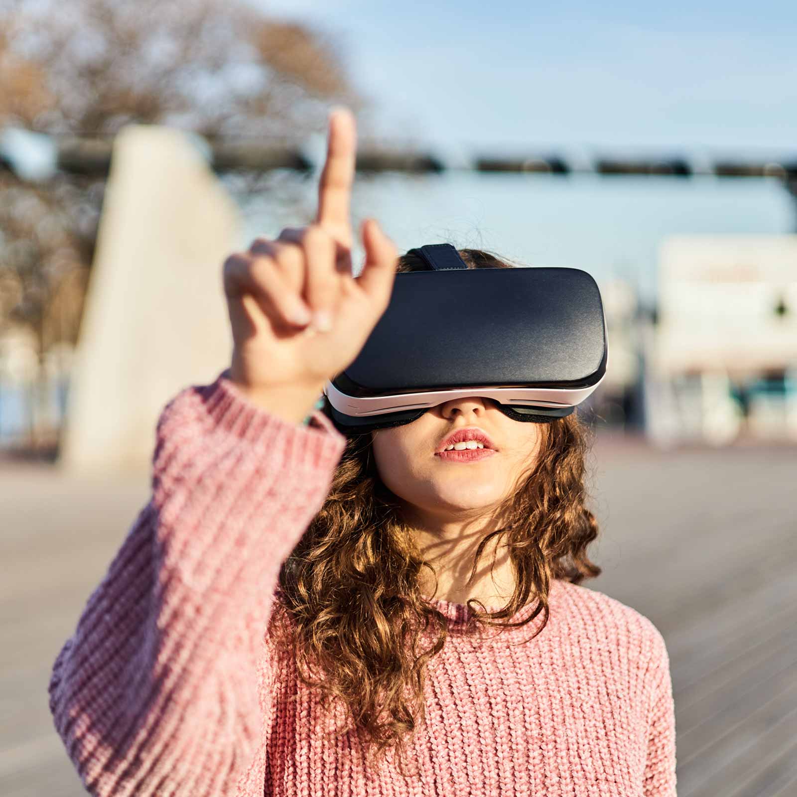 Young woman wearing a pink sweater and a VR headset outdoors