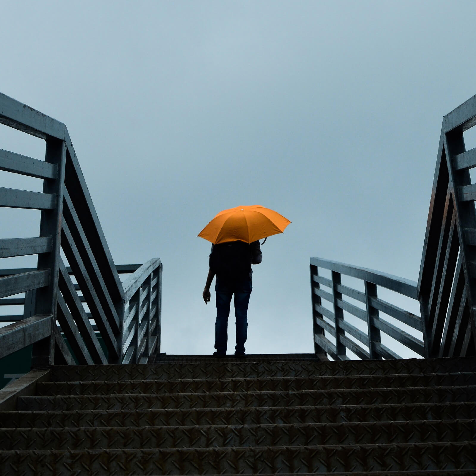 Silhouette of a person stood at the top of some outdoor steps holding an orange umbrella