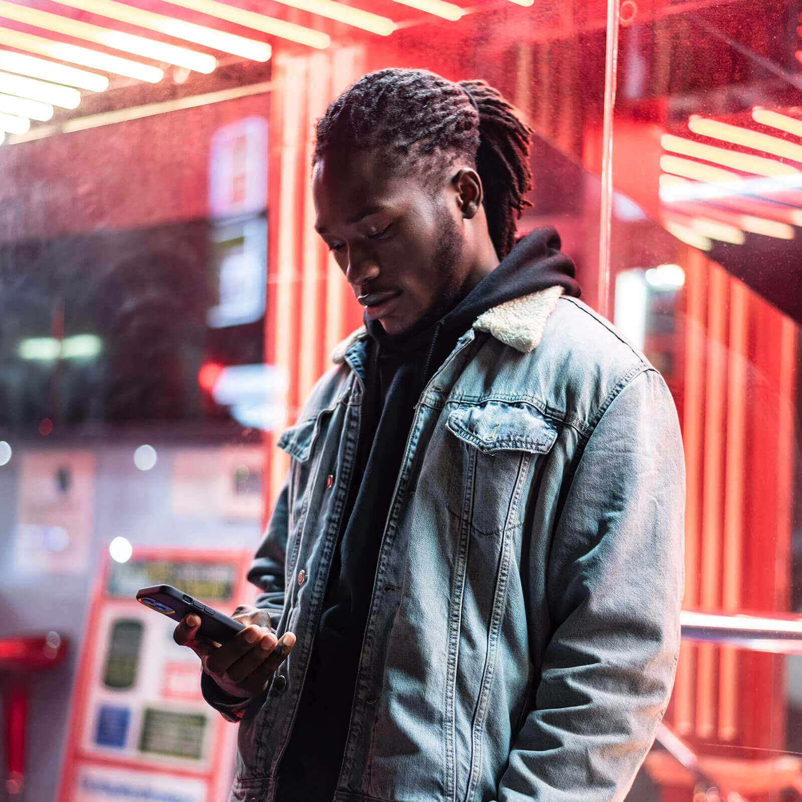 Man looking down at phone stood in front of neon lights