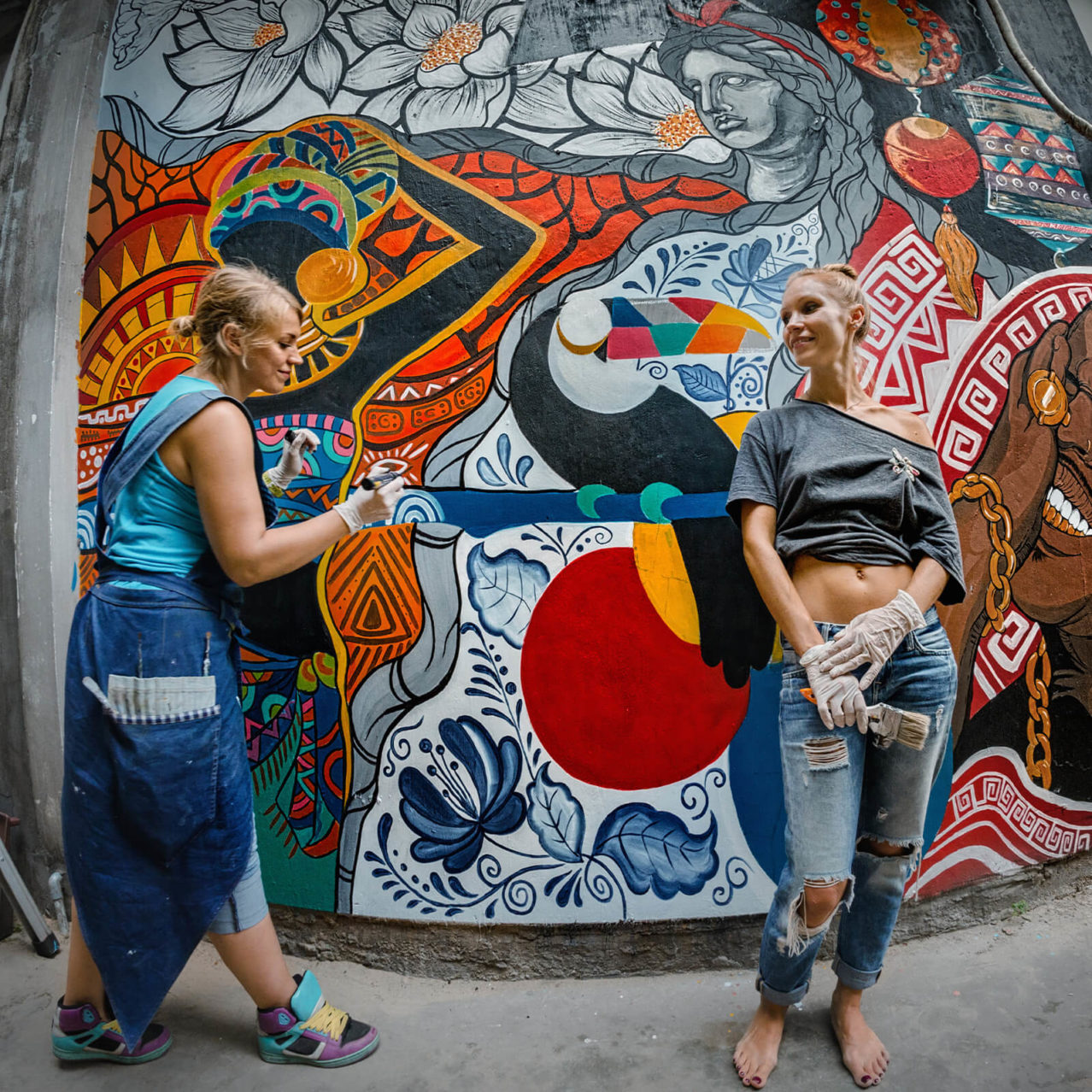 2 woman painting a mural outdoors on a large wall