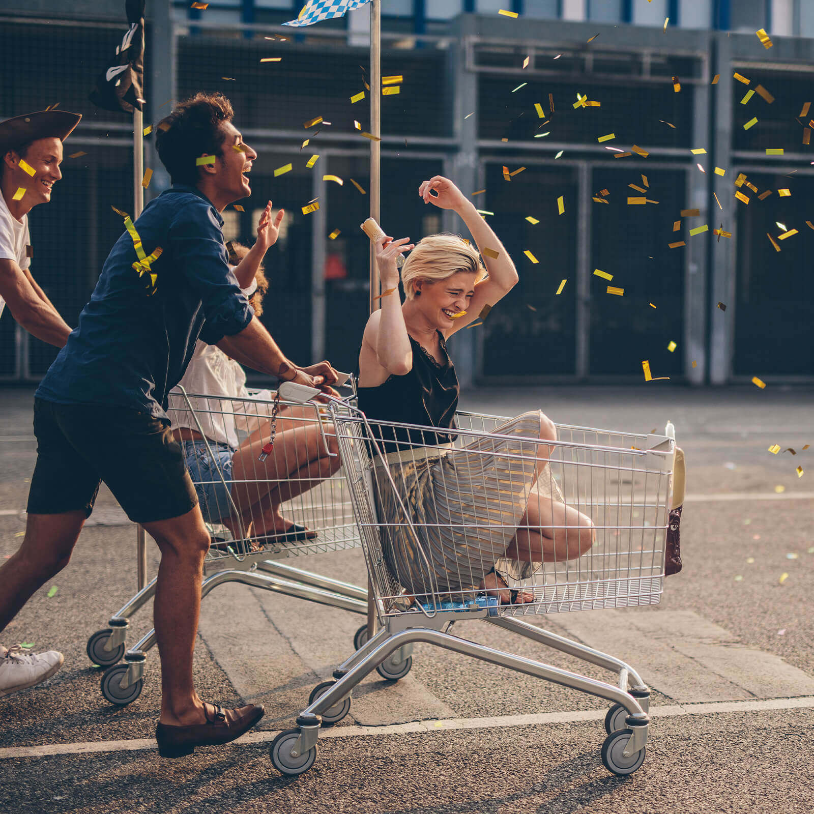 Group of friends having fun with one person pushing another in a shopping trolley.