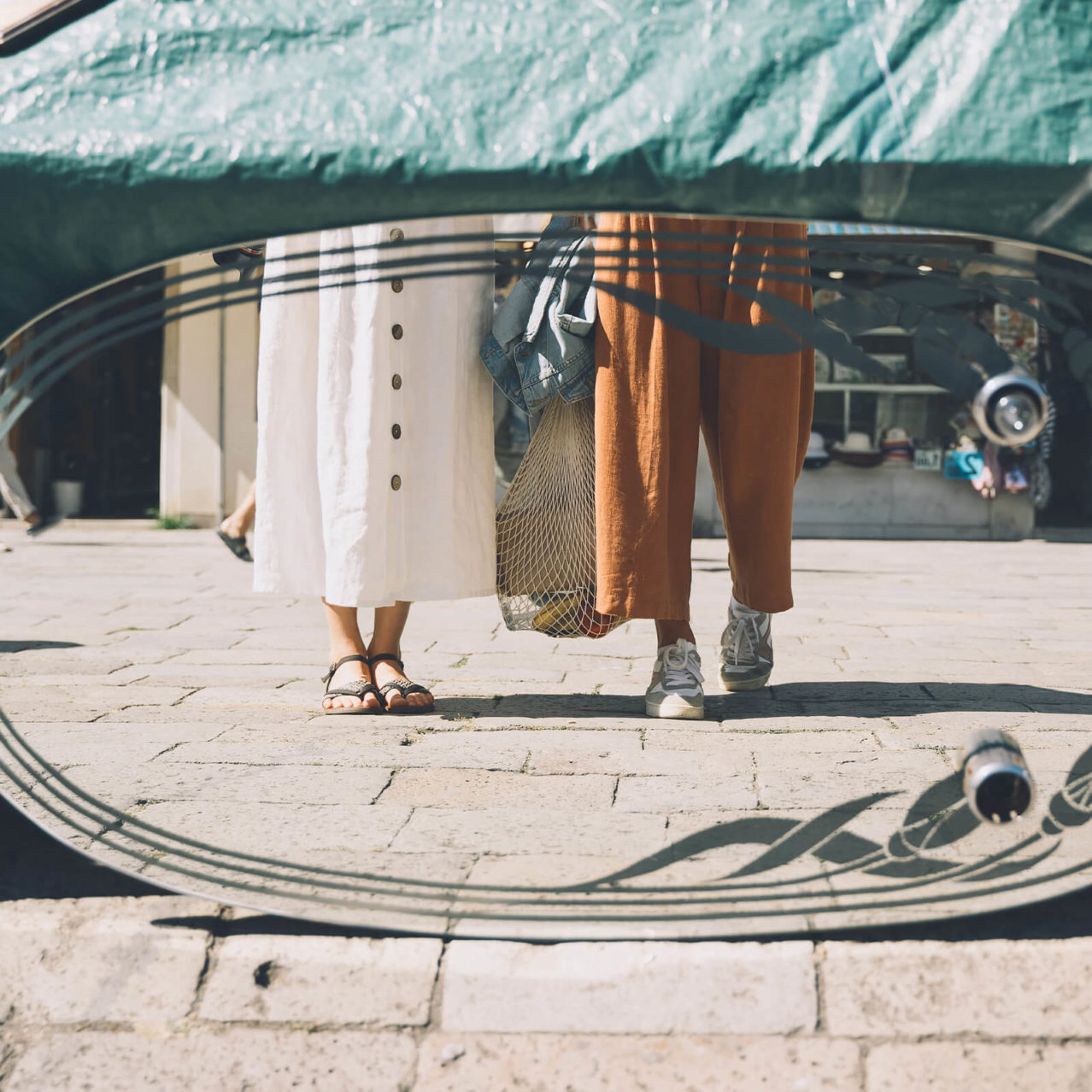 Mirror at a vintage market reflecting the legs of two people. One is carrying a shopping bag.