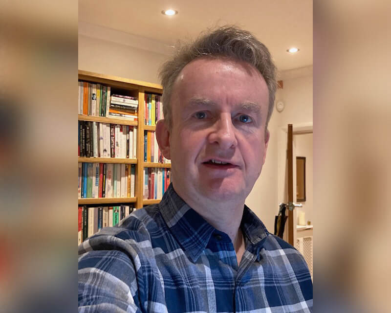 A man taking a selfie in front of a full bookcase